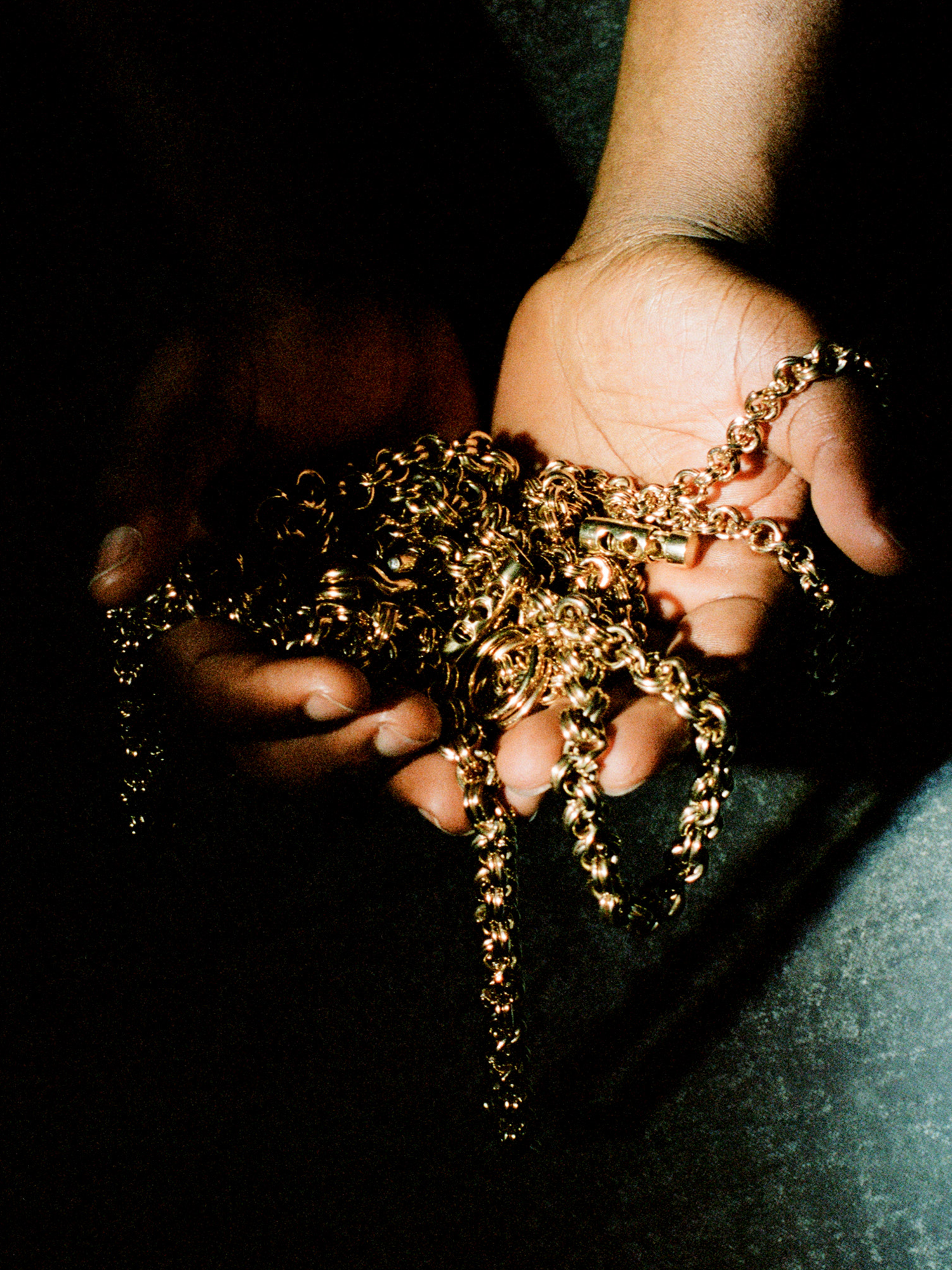 Hands holding gold chains against a dark background