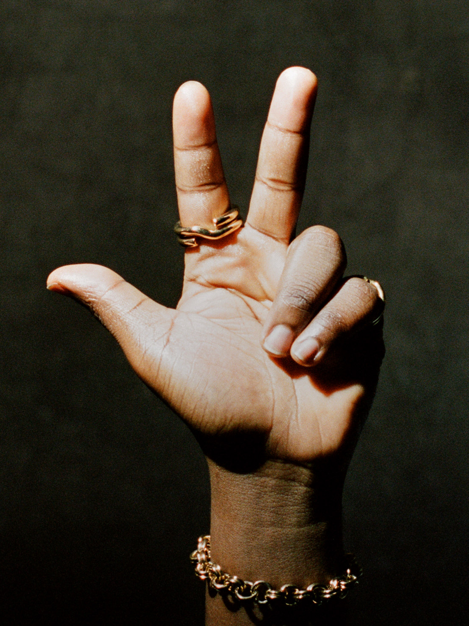 Hand with gold rings and bracelet on a dark background